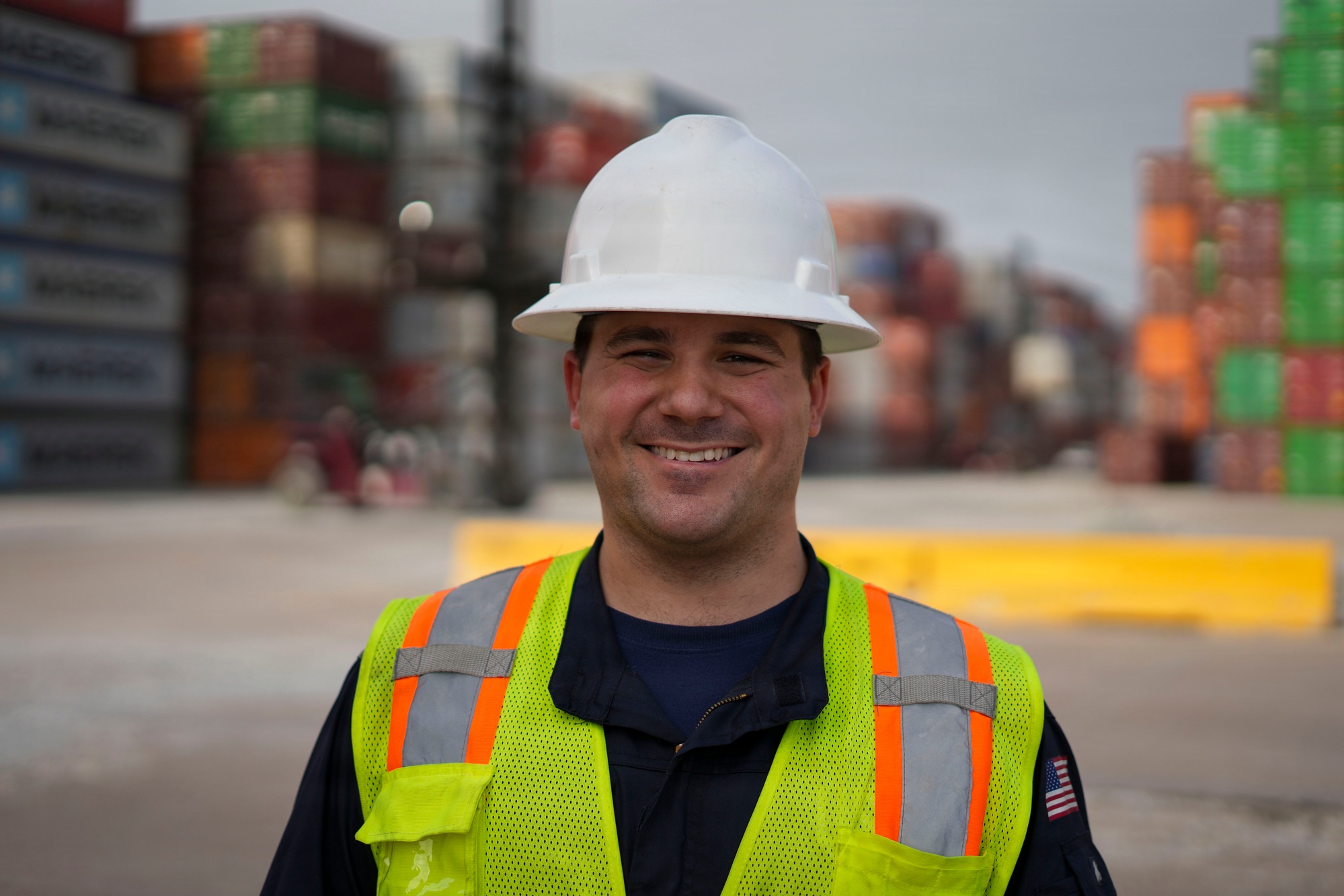 A worker in a white hard hat stands in front of stacked containers at Barbours Cut Container Terminal